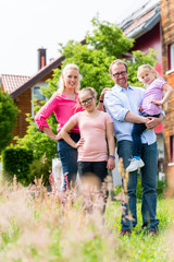 Mutter, Vater und Kinder stehen vor Haus, die ganze Familie schaut in die Kamera