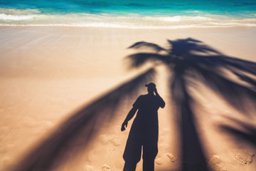 Fototapeta na wymiar Man and palm tree shadows on tropical white sand beach