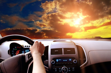 Driver's hands on a steering wheel of a car and blue sky