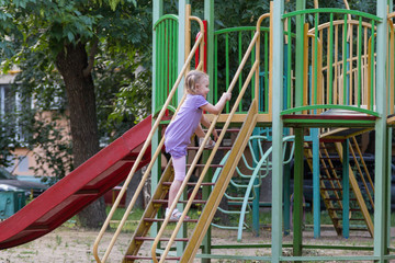 Fototapeta premium little girl with a ponytail climbs the stairs to the slide