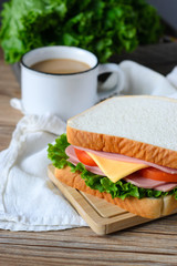 sandwich with ham, cheese and vegetables,and coffee on wood table
