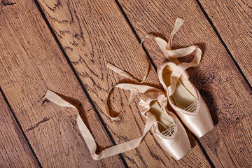 Ballet pointe shoes lie on wooden floor.