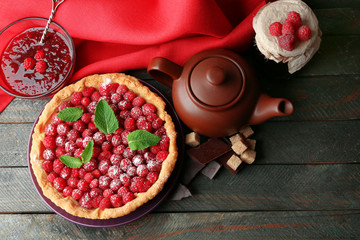 Tart with fresh raspberries and teapot, on wooden background