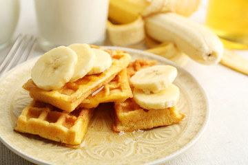 Sweet homemade waffles with sliced banana on plate, on light background