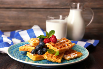 Sweet homemade waffles with forest berries and sauce on table background