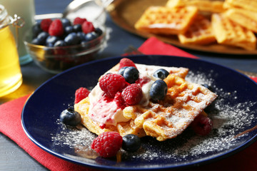 Sweet homemade waffles with forest berries and cream on plate, on dark wooden background