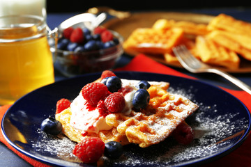 Sweet homemade waffles with forest berries and cream on plate, on dark wooden background