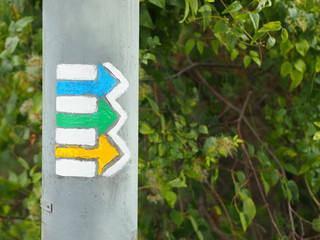 Yellow, green and blue tourist arrows pointing to the right drawn on an electricity pole in the czech countryside.