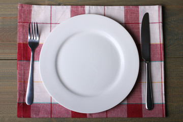 fork and knife next to the plate on napkin on wooden table
