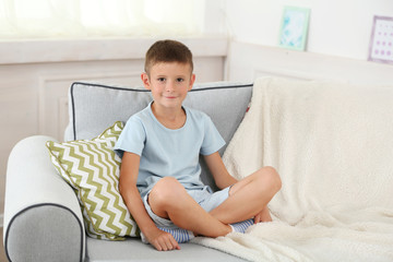 Little boy sitting on sofa, on home interior background