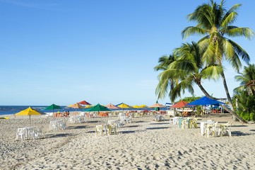 Palm trees stand over rustic village beach with beach chairs and umbrellas on the northeast Nordeste coast of Brazil