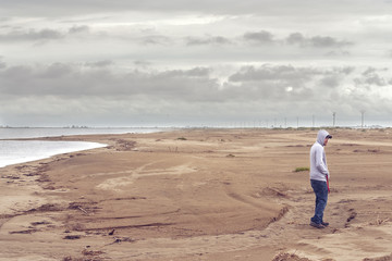 Young man on the beach wearing a hoodie and a baseball cap