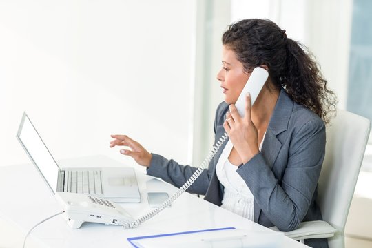 Confident pregnant businesswoman talking on phone while working