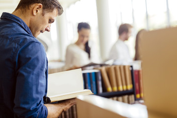 Fototapeta premium Handsome student reading a book in a library