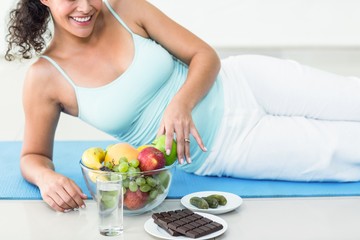Obraz na płótnie Canvas Smiling pregnant woman lying by fruits and chocolates