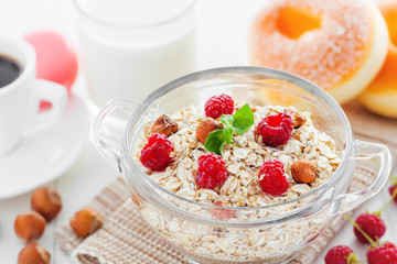 Healthy food. Oatmeal muesli with raspberry and hazelnut, coffee and doughnut on white table.