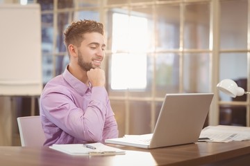Naklejka premium Biznesmen z ręką na brodzie pracy z laptopem