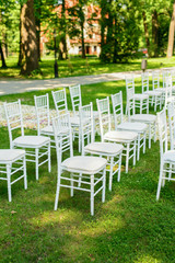 White wedding chairs set up and petals on green grass before the ceremony