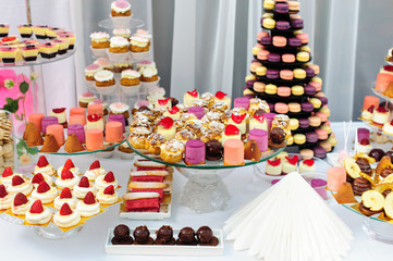 Wedding decoration with colorful cupcakes, eclairs, souffle, meringues, muffins and macarons. Elegant and luxurious event arrangement with sweets. Wedding dessert table