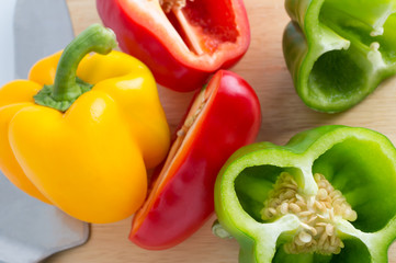 Red, yellow, green bell pepper with knife on cutting board