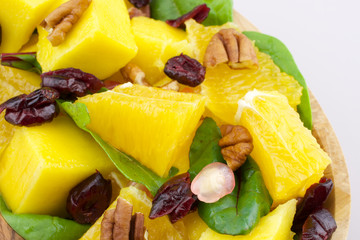 Fruit salad - mango, orange, pomegranate, nuts, cranberries - on wooden plate