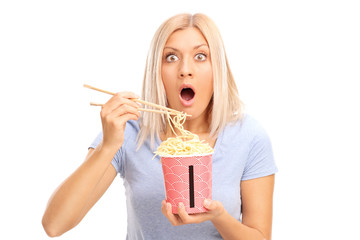 Shocked blond woman eating Chinese noodles