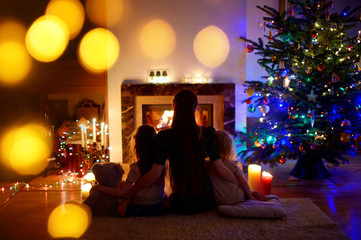 Young mother and daughters sitting by a fireplace on Christmas