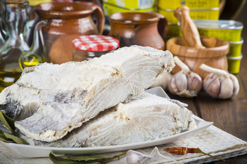 Lomo de bacalao salado cortado, pescado seco en la mesa de la cocina con ingredientes para cocinar.