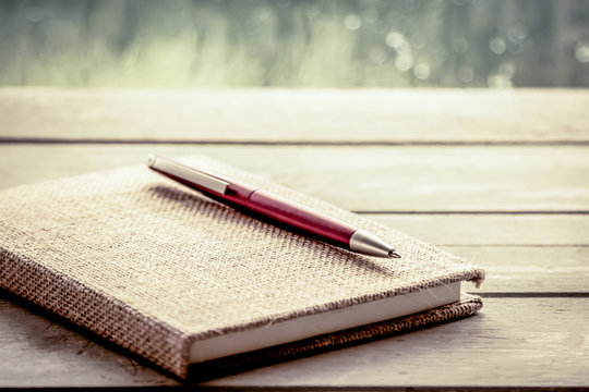 Pen On Notebook On Wooden Table In Rainy Day Window Background,