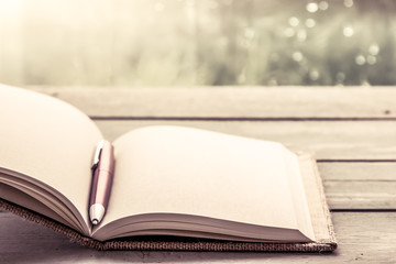 Pen on open notebook on wooden table in rainy day 