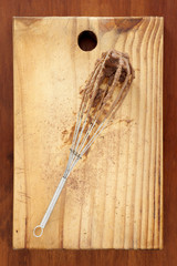 Whisk with chocolate. Metallic whisk with chocolate over cutting board for baking concept.