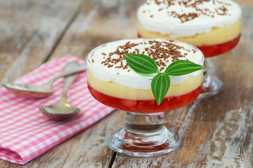 Traditional English strawberry trifle in transparent dessert glass on rustic wooden surface

