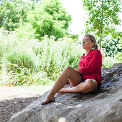 sad young woman sitting on giant stone for summer freshness