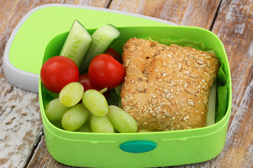 Healthy school lunch box containing whole grain roll with cheese and lettuce, grapes, cherry tomatoes and cucumber sticks
