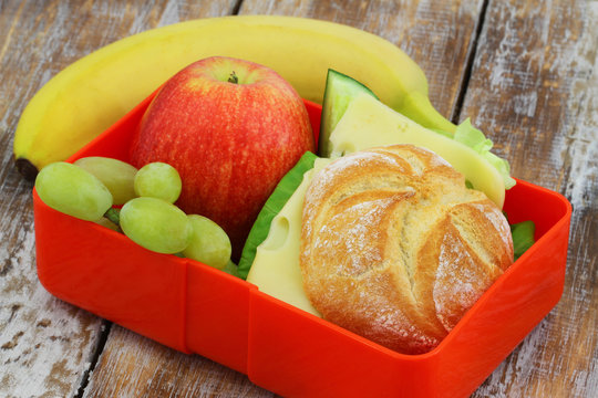 School lunch box containing cheese roll, apple, grapes and banana
