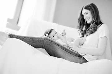 Playfull mother with her beloved daughter on white sofa in white bedroom, near window, lightly...