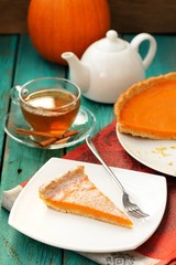 Pumpkin pie, tea in glass cup, white teapot and fresh pumpkin on