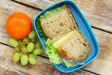 Healthy lunch box containing rustic bread sandwiches with cheese and lettuce, grapes and mandarine 
