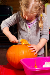 Kind kratzt mit einem Löffel einen Kürbis aus, bastelt einen Leucht Kürbis für Halloween daraus