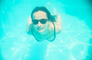 Girl swimming underwater in sunglasses