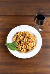 Wine and Italian pasta with basil on white plate on wooden table with shallow depth of field.