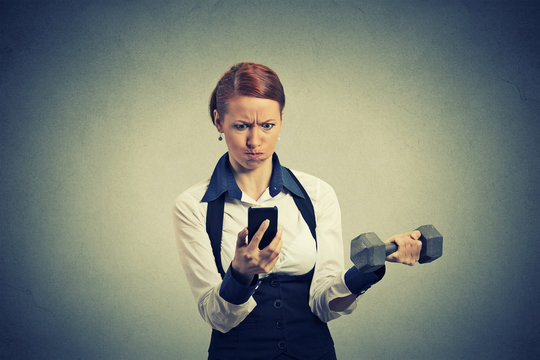 angry business woman reading news e-mail on mobile phone lifting dumbbell