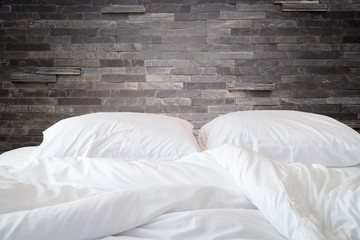 White bedding sheets and pillow on natural stone wall room backg