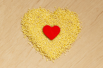 Millet groats heart shaped on wooden surface.