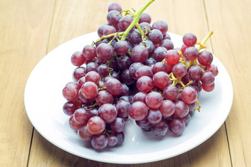 red bunch grape in white dish on wooden board