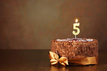 Birthday chocolate cake with burning candle as a number five on brown background