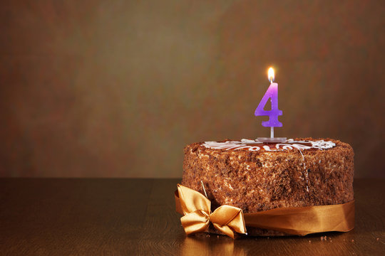 Birthday chocolate cake with burning candle as a number four on brown background