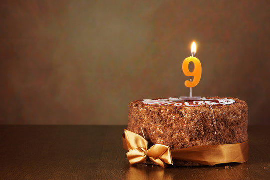 Birthday chocolate cake with burning candle as a number nine on brown background
