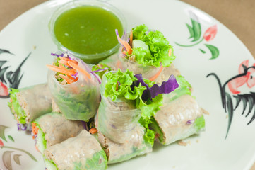 Portion of spring rolls on old wood with spicy sauce, vegetables