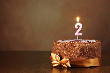 Birthday chocolate cake with burning candle as a number two on brown background
